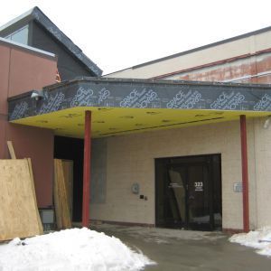 Entrance to a building with a yellow canopy supported by red pillars. Snow on the ground.