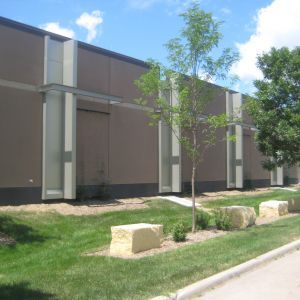 Tan building exterior with vertical light-colored accents, landscaping, and a blue sky.