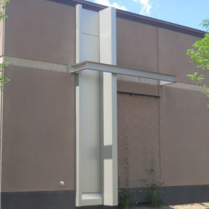 Modern building exterior with a vertical silver architectural element, topped with a horizontal canopy.