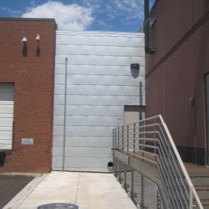 Exterior view of three connected buildings: brick, silver metal, and brown with a ramp and sky.