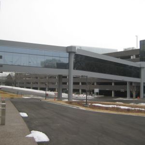 Pedestrian bridge connects a parking garage to a building. Gray, modern architecture. Asphalt road with snow.