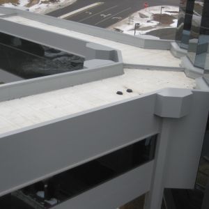 Overhead view of a white, multi-level building roof with a pathway, overlooking a street with a snowy background.
