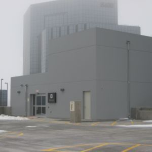 Gray building with a small entrance, on a rooftop with a tall building obscured by fog in the background.