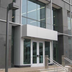 Modern building entrance with double glass doors, a white overhang, and silver metal accents.