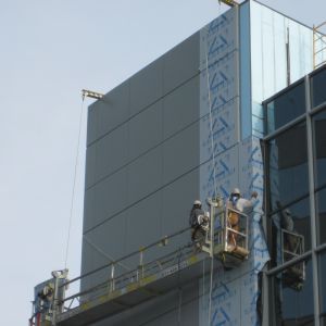 Construction workers in a suspended scaffold installing exterior panels on a high-rise building.