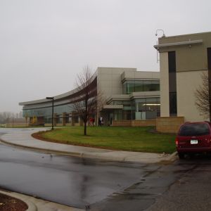 Modern building with curved glass facade, red minivan parked on the side, overcast sky.
