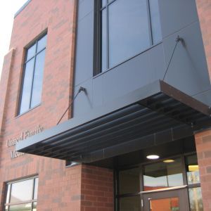Brick building entrance with a black awning and large windows.