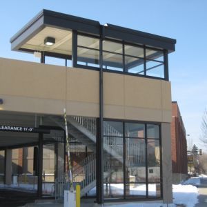 Exterior of a two-story building with a stairwell. Tan and black building with a glassed-in office on top.