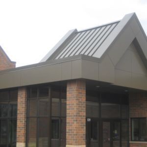 Brown building entrance with brick columns, glass doors, and a metal roof.