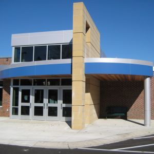 School entrance with blue and silver trim, tan pillar, and glass doors under a curved overhang.