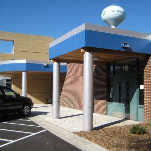 Building entrance with blue and silver awning; water tower in background; car parked.