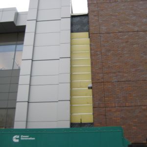 Building exterior with exposed insulation between brick and metal paneling.