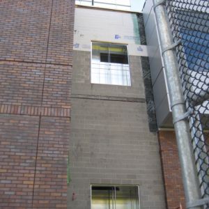 Exterior building walls; brick, concrete block, siding, with a window and a chain-link fence.