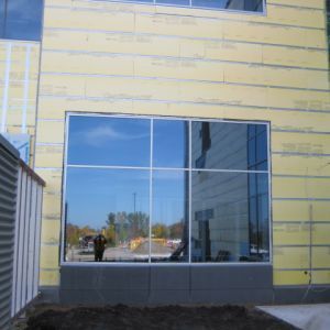 Large window on building under construction, reflecting blue sky and nearby structures.