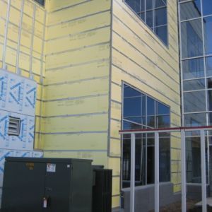 Exterior of a building under construction, showing yellow insulation boards and glass windows.