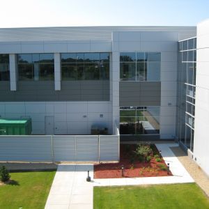 Modern building with gray and white exterior, windows, and small landscaping area.