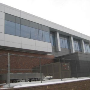Modern building with large windows and brick base, behind a chain-link fence.