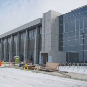 Modern building under construction with glass facade, snow, and construction equipment.