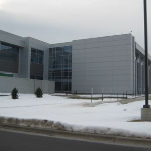 Modern gray building with large windows and snow-covered ground in front.