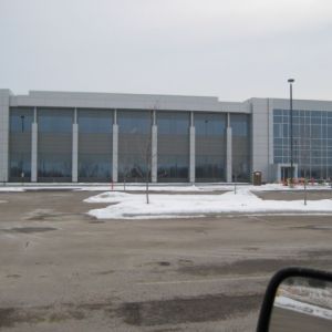 Modern building with large windows, snow on ground in front, overcast sky.