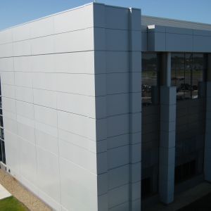 Modern building exterior with light gray metal panels and glass windows.