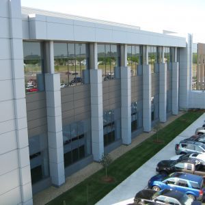 Modern building exterior with large windows, silver facade, and a row of parked cars.