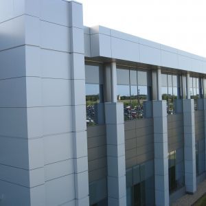 Modern building with light gray and silver facade, large windows, and vertical columns.