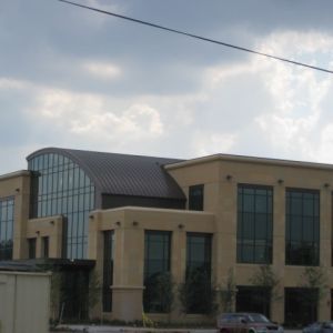 Tan two-story building with a curved roof and large windows under a cloudy sky.