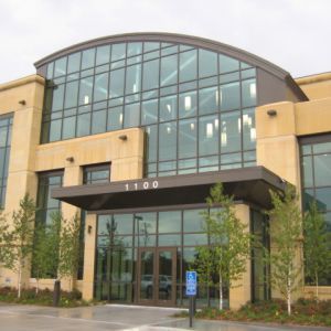 Modern building with large glass windows and arched roof, tan exterior, entrance with canopy.