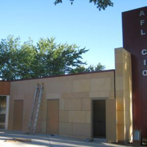 Building with tan stone facade, ladder, and a sign for AFL-CIO. Clear sky.