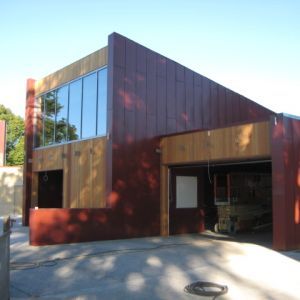 Modern building with garage, large windows, and reddish-brown and wood siding.