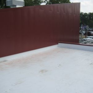 View of a flat roof with a tall, maroon-colored wall and a white surface; outdoors.