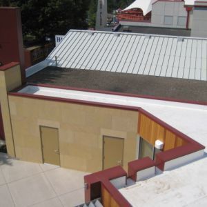 View of building rooftops: beige and white surfaces, metal roof, red trim, two tan doors, stairs.