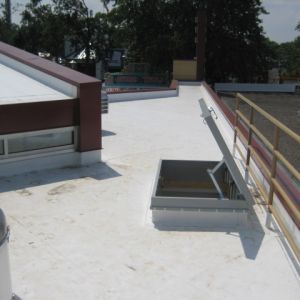 White flat roof with open access hatch, next to a building with red trim.
