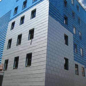 Exterior view of a building with blue and silver siding, rectangular windows.
