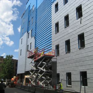 Construction workers on a scissor lift installing siding on a multi-story building. Blue and grey siding. Sunny day.