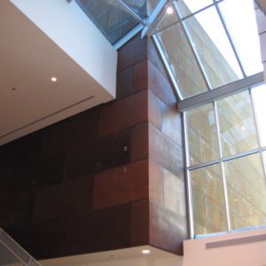 Brown paneled wall with a large window and angled glass ceiling.