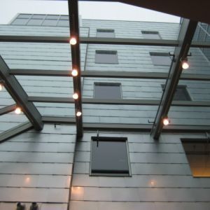 Metallic building exterior with horizontal panels, small windows, and overhead lighting fixtures.