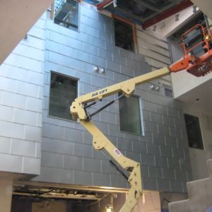 Construction site: yellow aerial lift installing silver paneling on building exterior.
