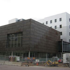Modern building with a dark, textured facade and large windows; construction materials and equipment visible.