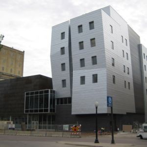 Modern building with angular, silver facade and dark base, street in front.