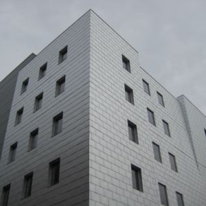 Silver-paneled modern building with rows of rectangular windows against a gray sky.