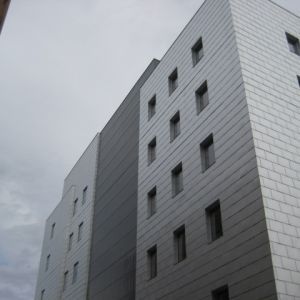 Modern multi-story building with a gray, tiled facade. Cloudy sky.