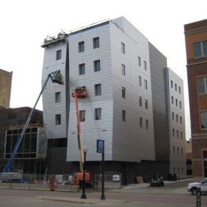 Building under construction with silver metal facade and construction lifts.