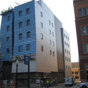 Building under construction with blue and metallic paneling, scaffolding, and workers.