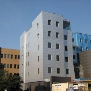 Modern light blue building with many windows, under a clear blue sky.