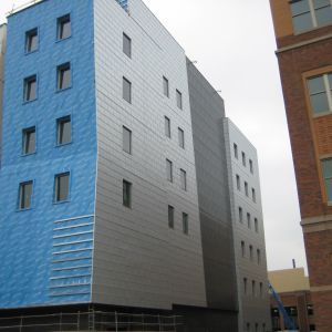 Multi-story building with blue protective wrap, gray panels, and windows under construction.