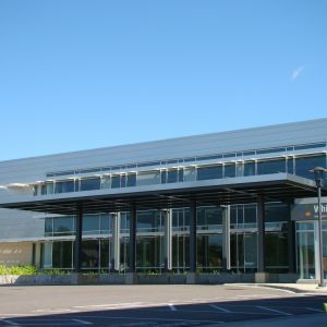 Modern building entrance with glass doors, canopy, and blue sky.