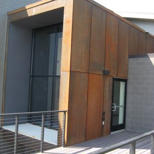 Modern building entrance with weathered brown metal siding and large glass windows.