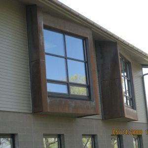 Exterior of a building with modern windows featuring large, dark frames set into a neutral-colored facade.